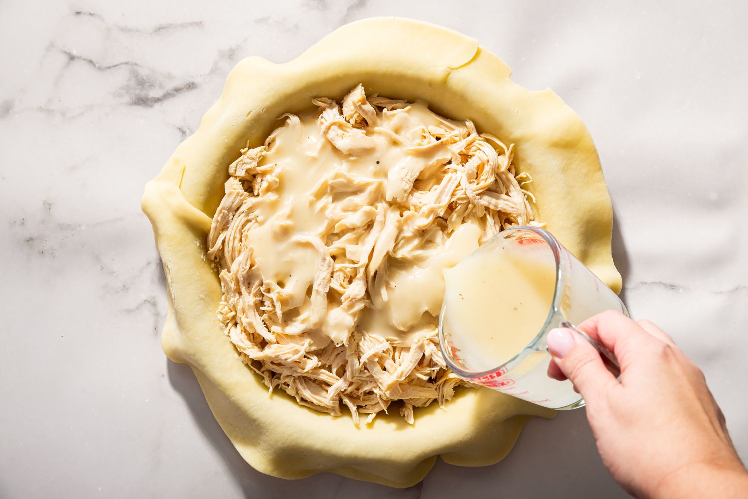 Overhead view of pouring the gravy into the shredded chicken and pie crust for Moravian Chicken Pie recipe