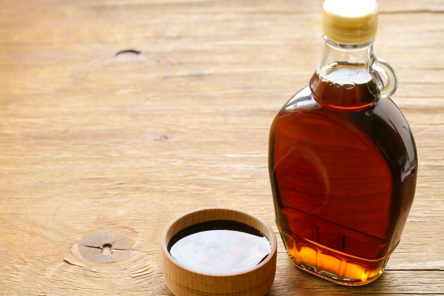 Bottle of syrup with a small bowl of syrup on a wooden surface