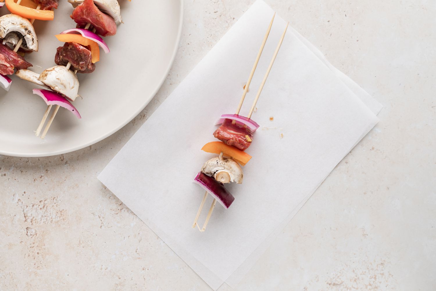 Layering meat and veggies to make beef kabobs.