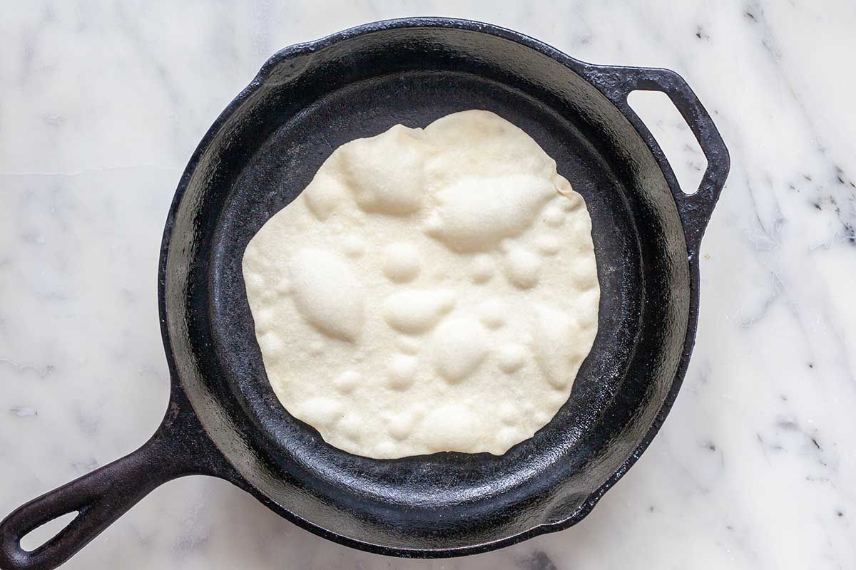 Easy homemade flour tortilla cooking in a cast iron skillet. It is pale and bubbly.