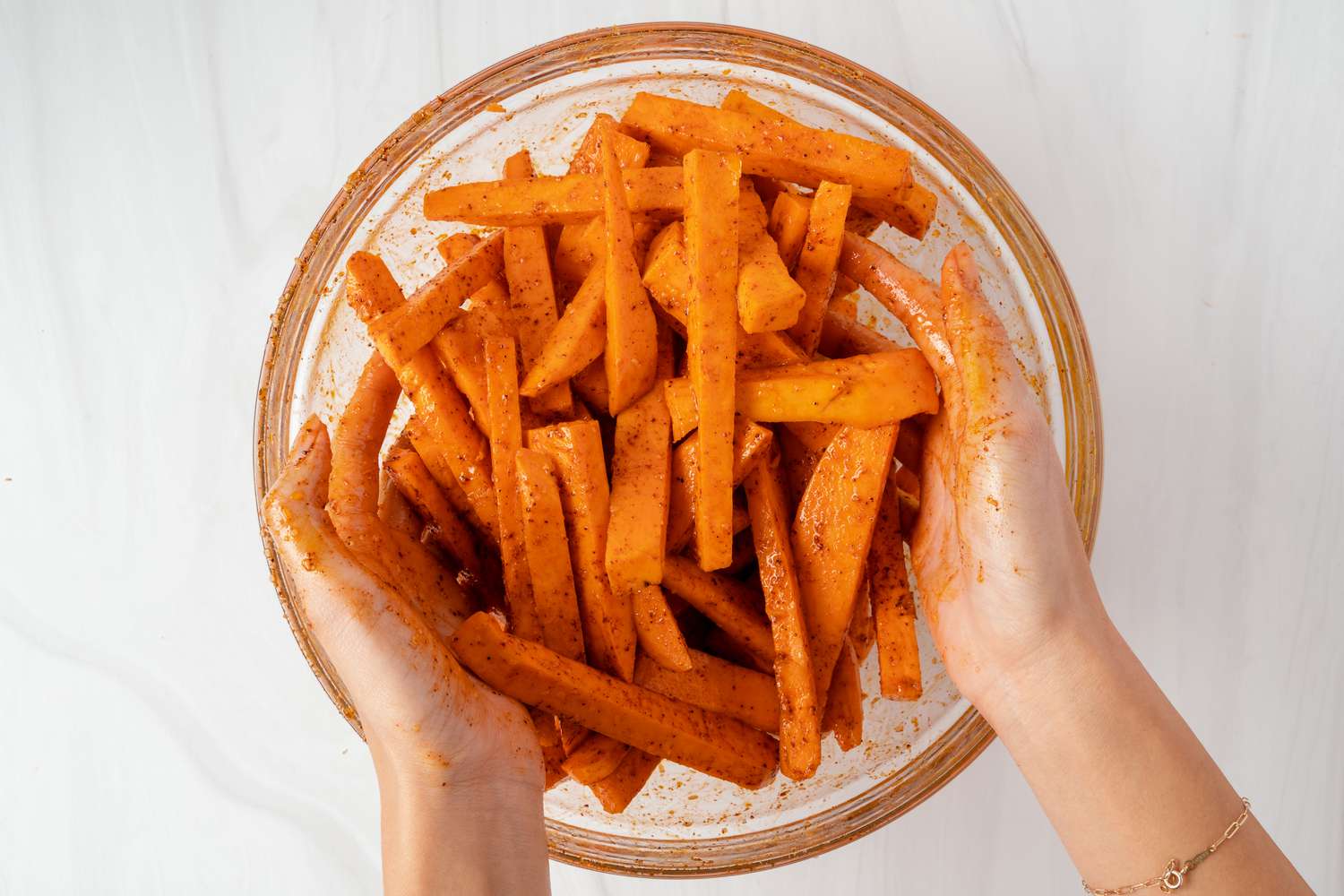 Tossing sweet potato wedges in seasoning in a glass bowl.