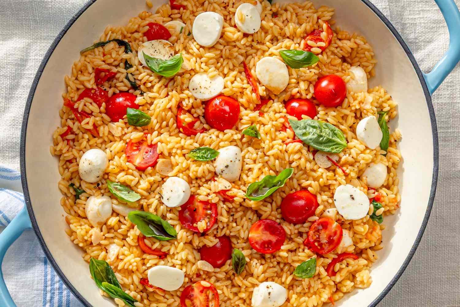 Dish featuring cooked orzo pasta with cherry tomatoes mozzarella and basil garnished on top