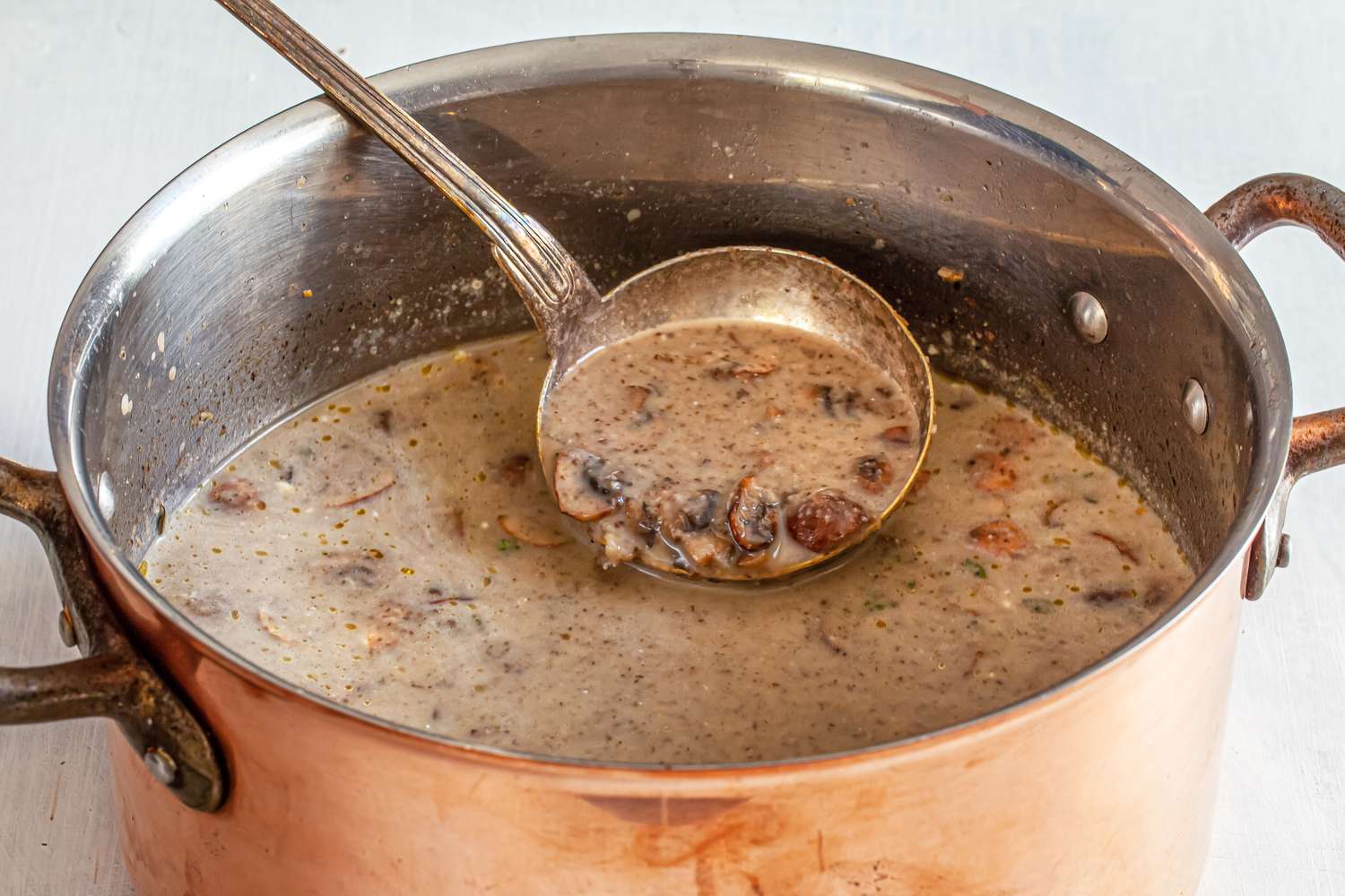 A large pot of cremini and chestnut soup with a ladle.