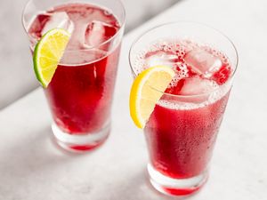 Two glasses of a red beverage garnished with lime and lemon wedges placed on a white surface