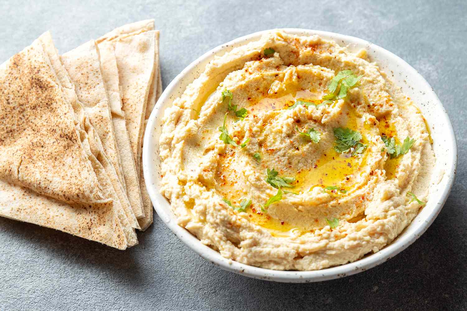 A bowl of hummus garnished with herbs and spices accompanied by pita bread