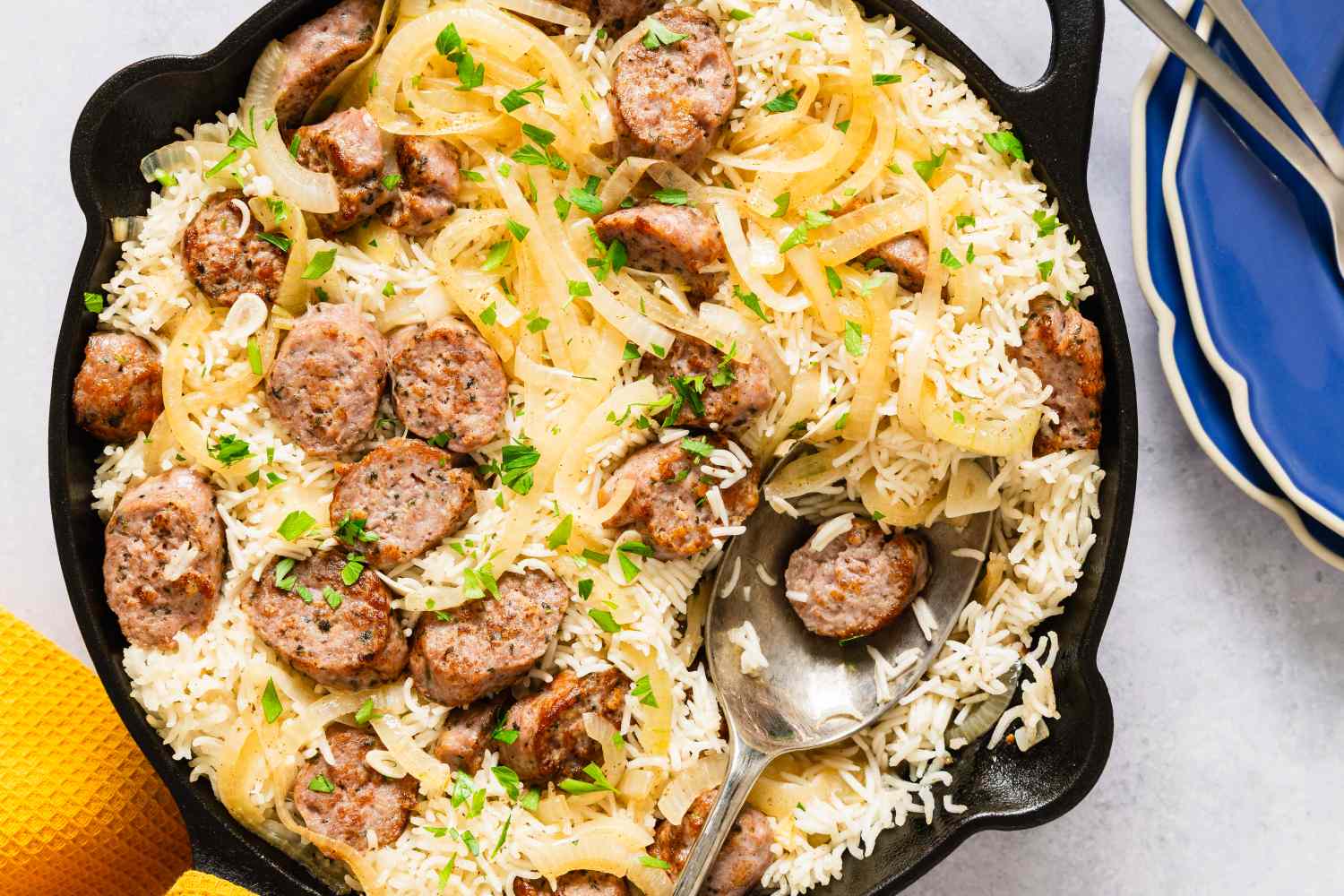 A skillet containing a sausage and rice bake with onions and fresh herbs a serving spoon resting inside