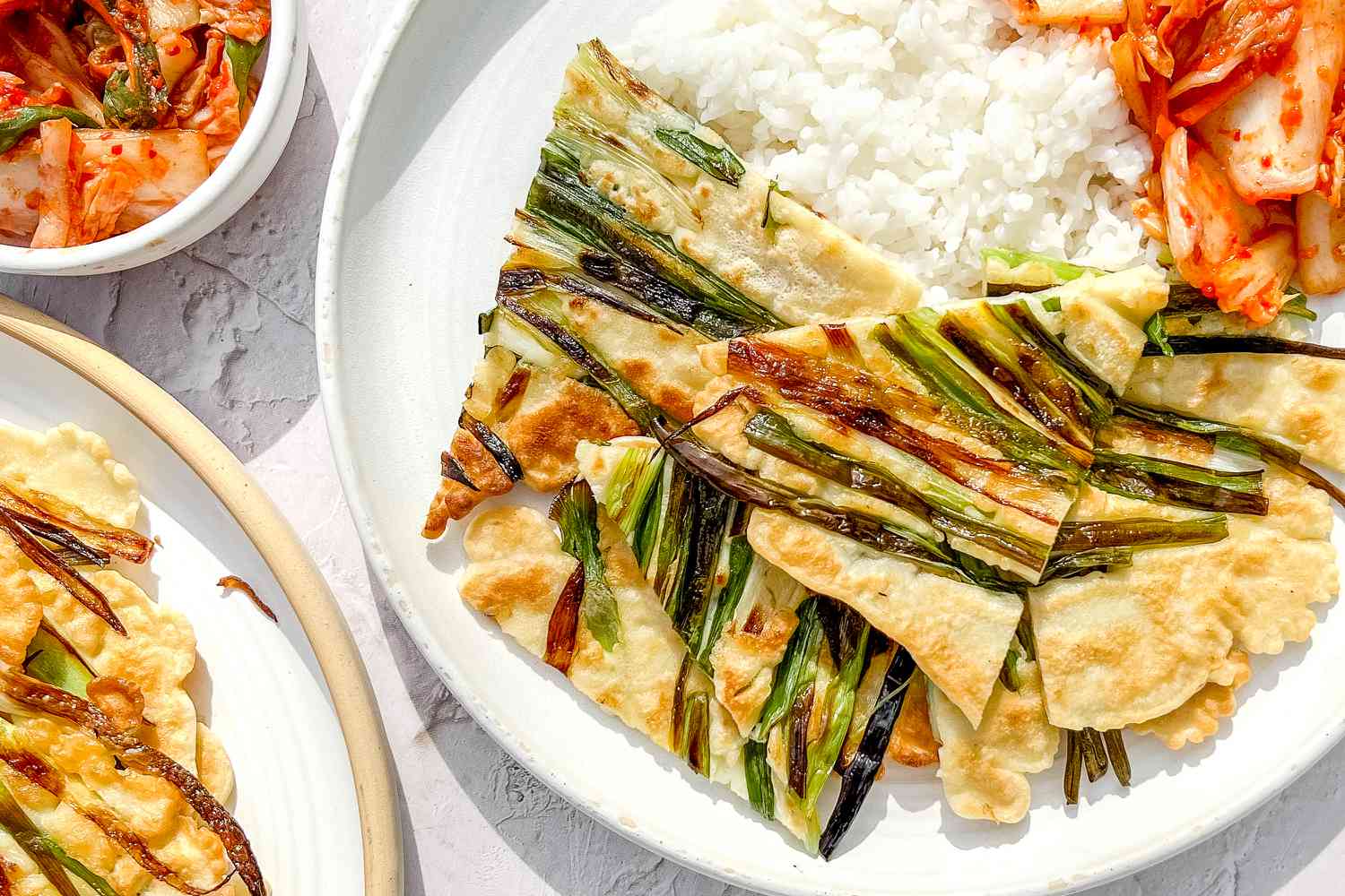 Pajeon, Kimchi, and Rice on a Plate Next to Another Plate of Pajeon and a Small Bowl of Kimchi