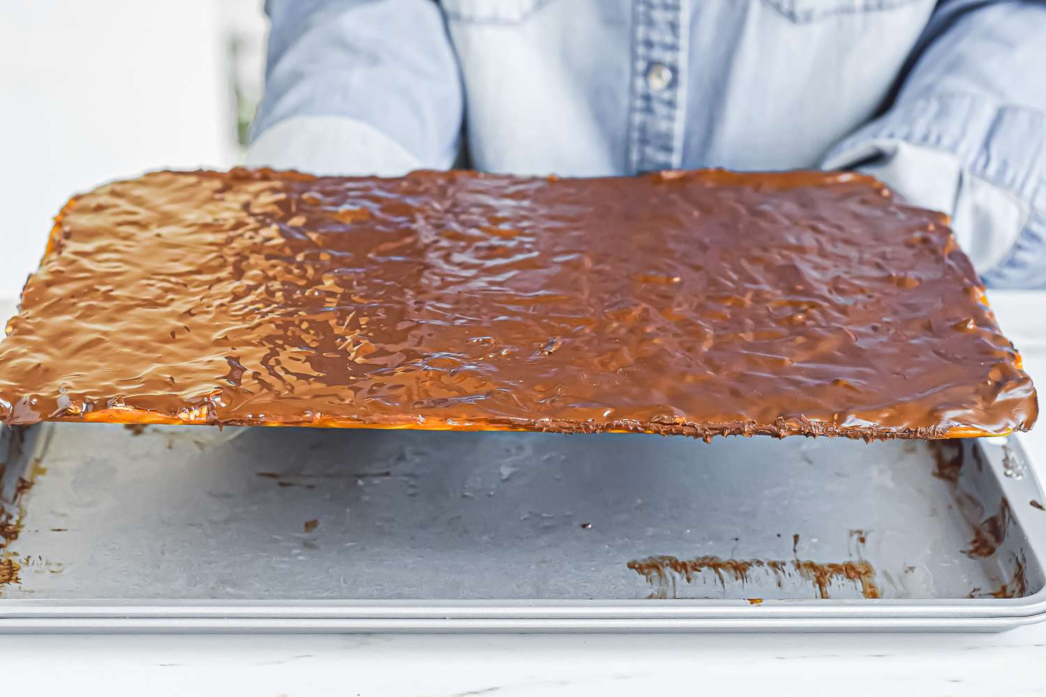 Lifting cooled almond roca up off the baking sheet.