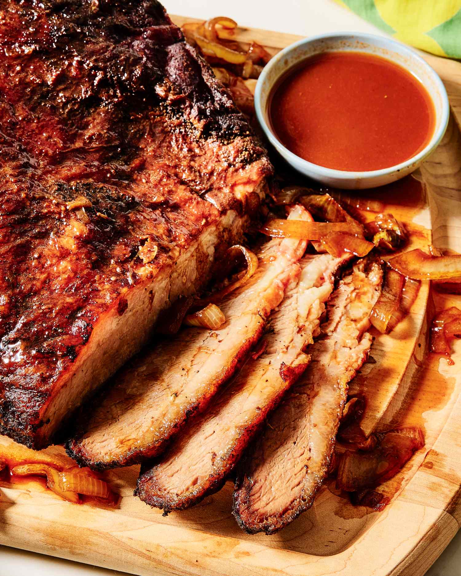 Sliced brisket on a wooden board with a bowl of sauce on the side