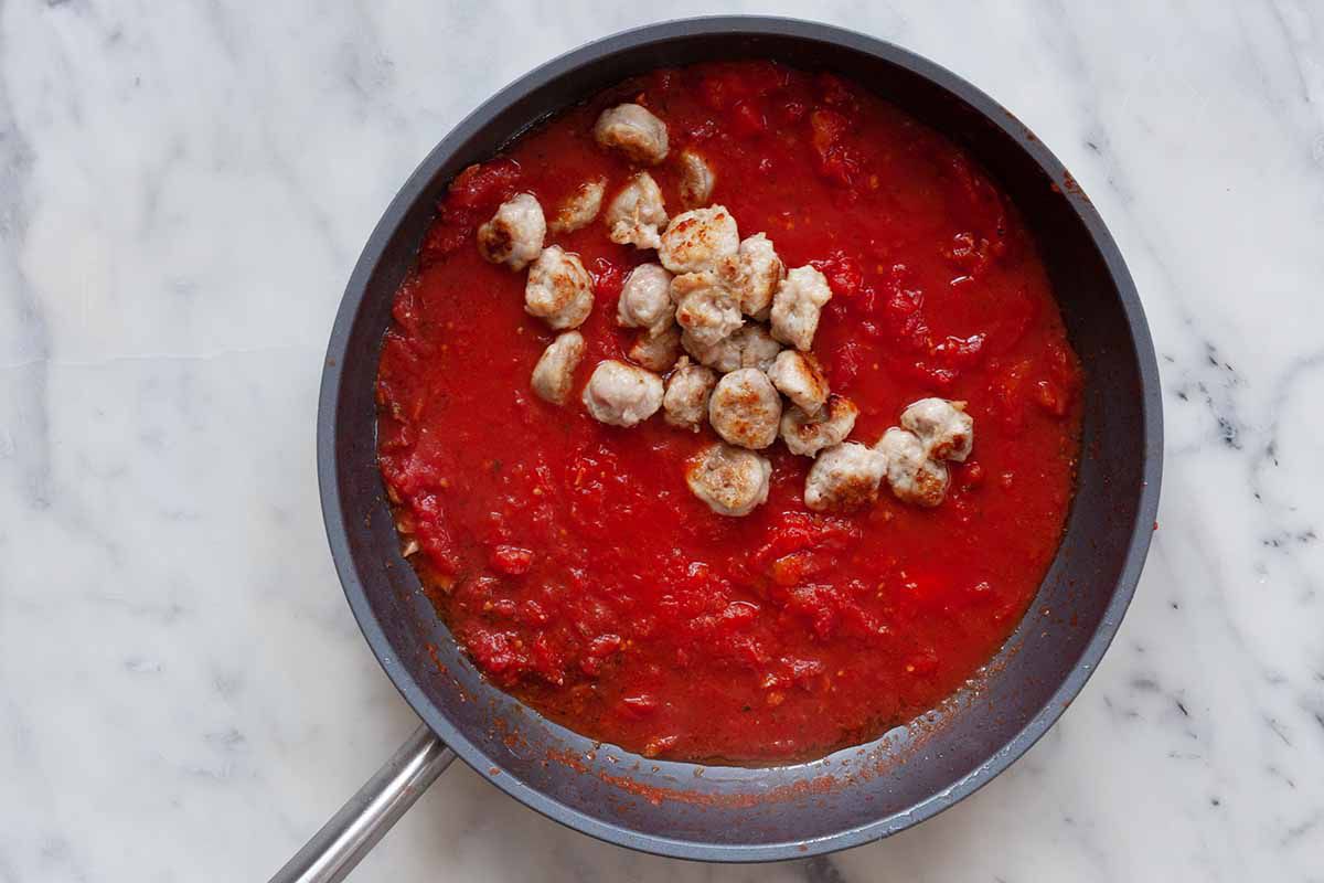 A skillet is filled with chunky tomato sauce and sliced italian sausage.