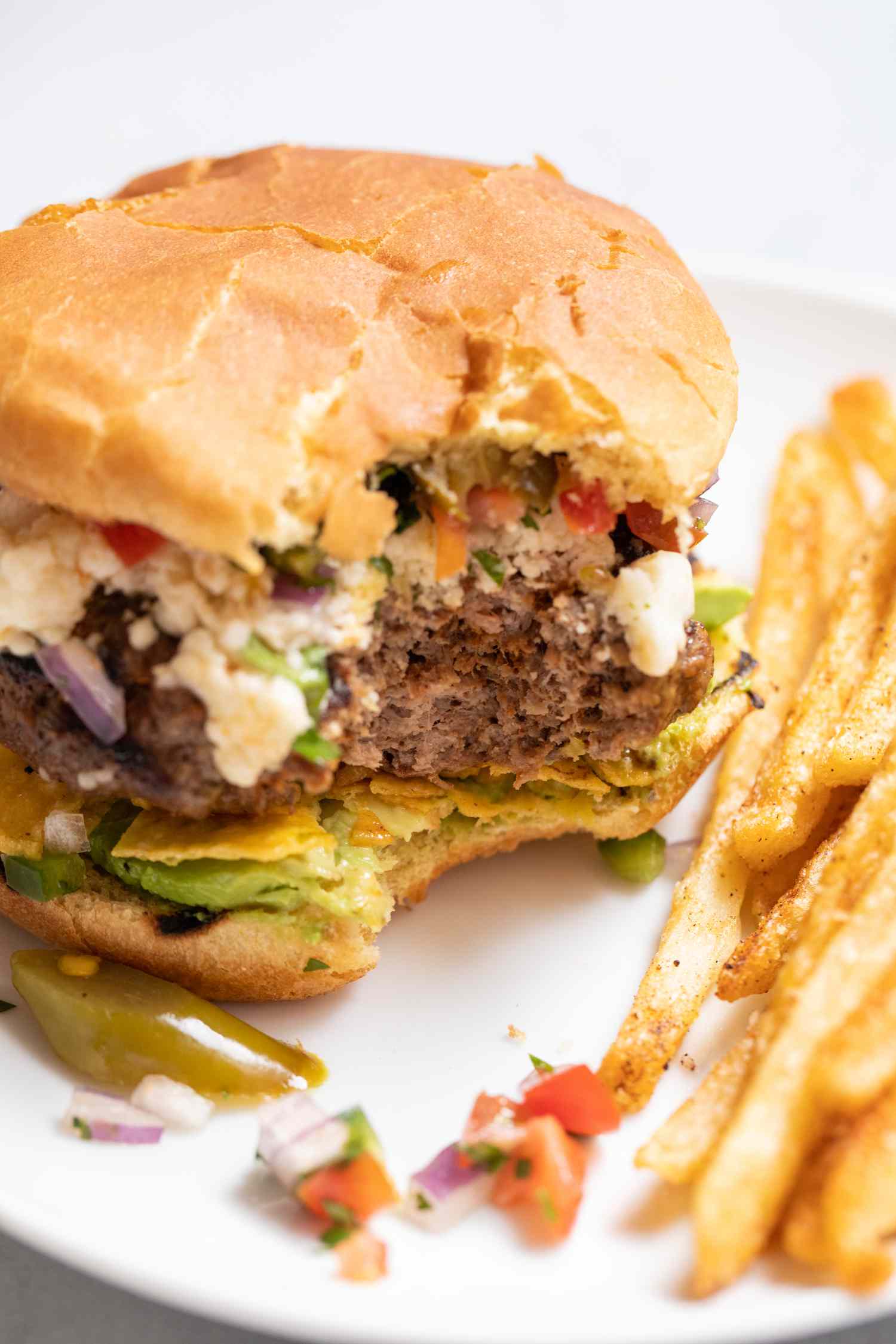 Mexican burger on a plate with a bite taken out and fries on the side.