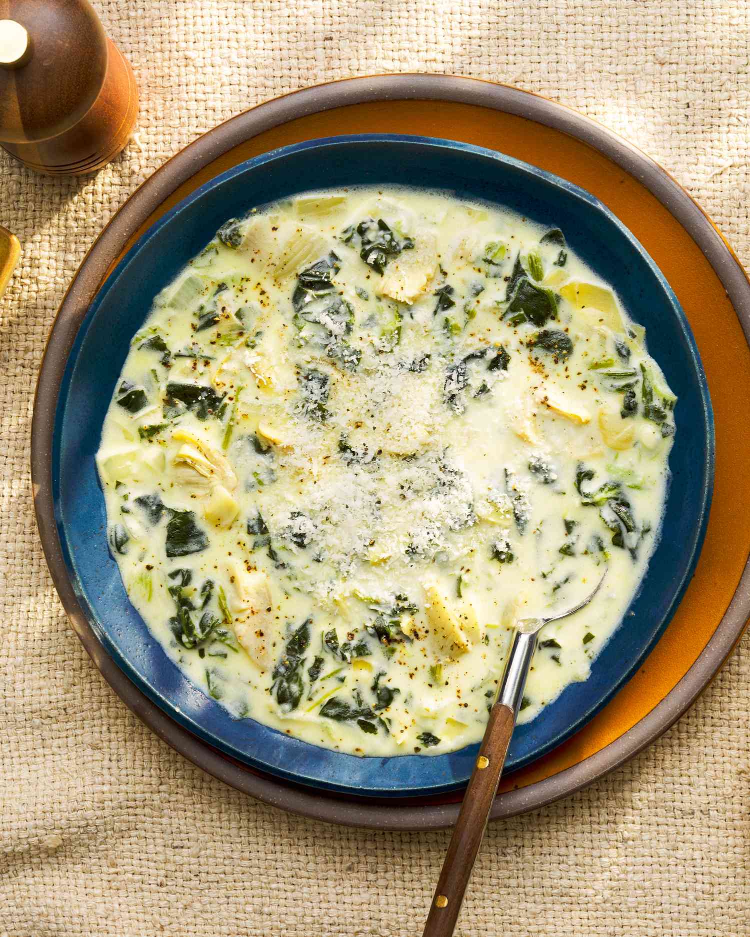 Overhead view of a bowl of spinach artichoke dip soup on a plate next to a pepper cracker