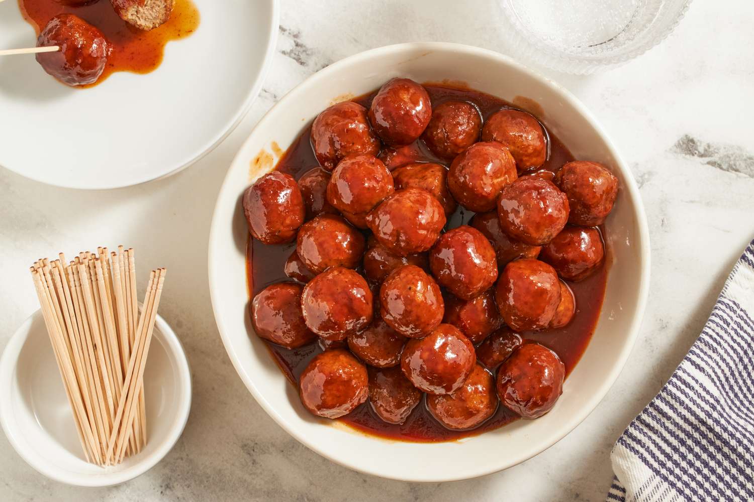 A bowl of saucy cocktail meatballs with a dish of toothpicks nearby