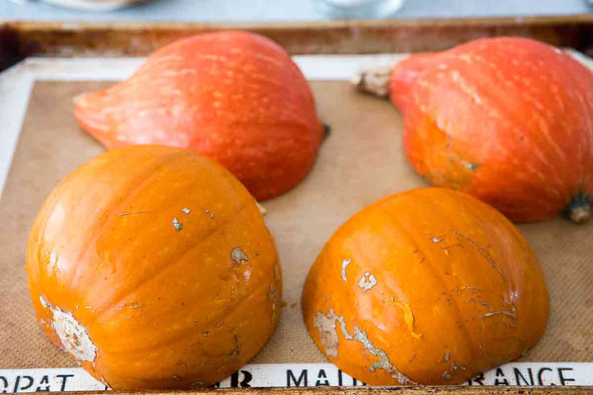 cut sugar pumpkins kabocha squash in half, scoop out seeds, place cut side down on lined baking sheet