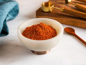 Small bowl of chili powder on a counter with measuring spoons and a small spoon
