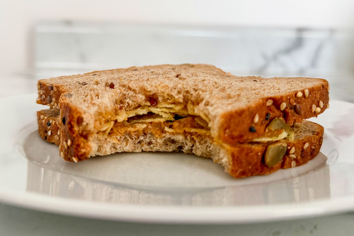 A sandwich with a bite taken out featuring seeded bread on a white plate