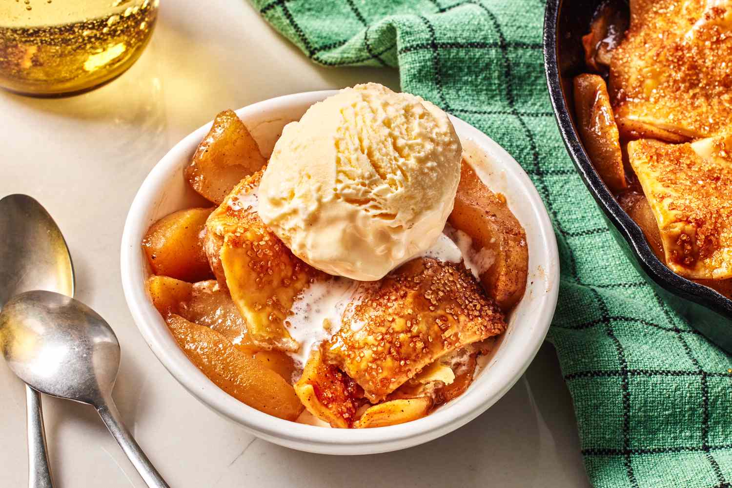 A white bowl with a serving of Apple Pandowdy topped with a scoop of vanilla ice cream