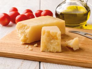 blocks of parmesan on a cutting board and in the background, grape tomatoes and a carafe of olive oil