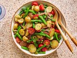 Sicilian potato salad in a bowl with serving utensils and next to a glass of water