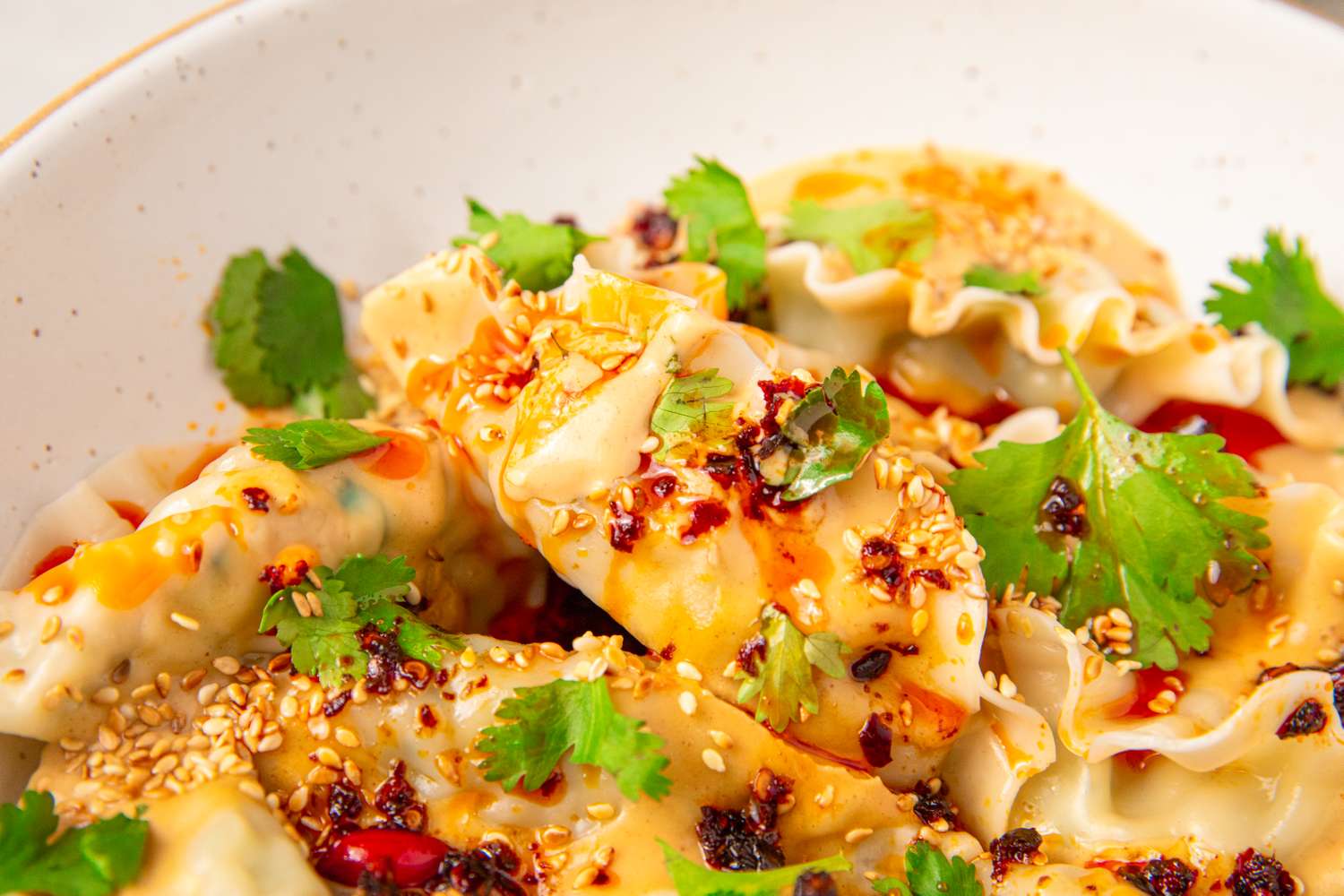A dish of peanut-chili dumplings garnished with cilantro and chili crisp