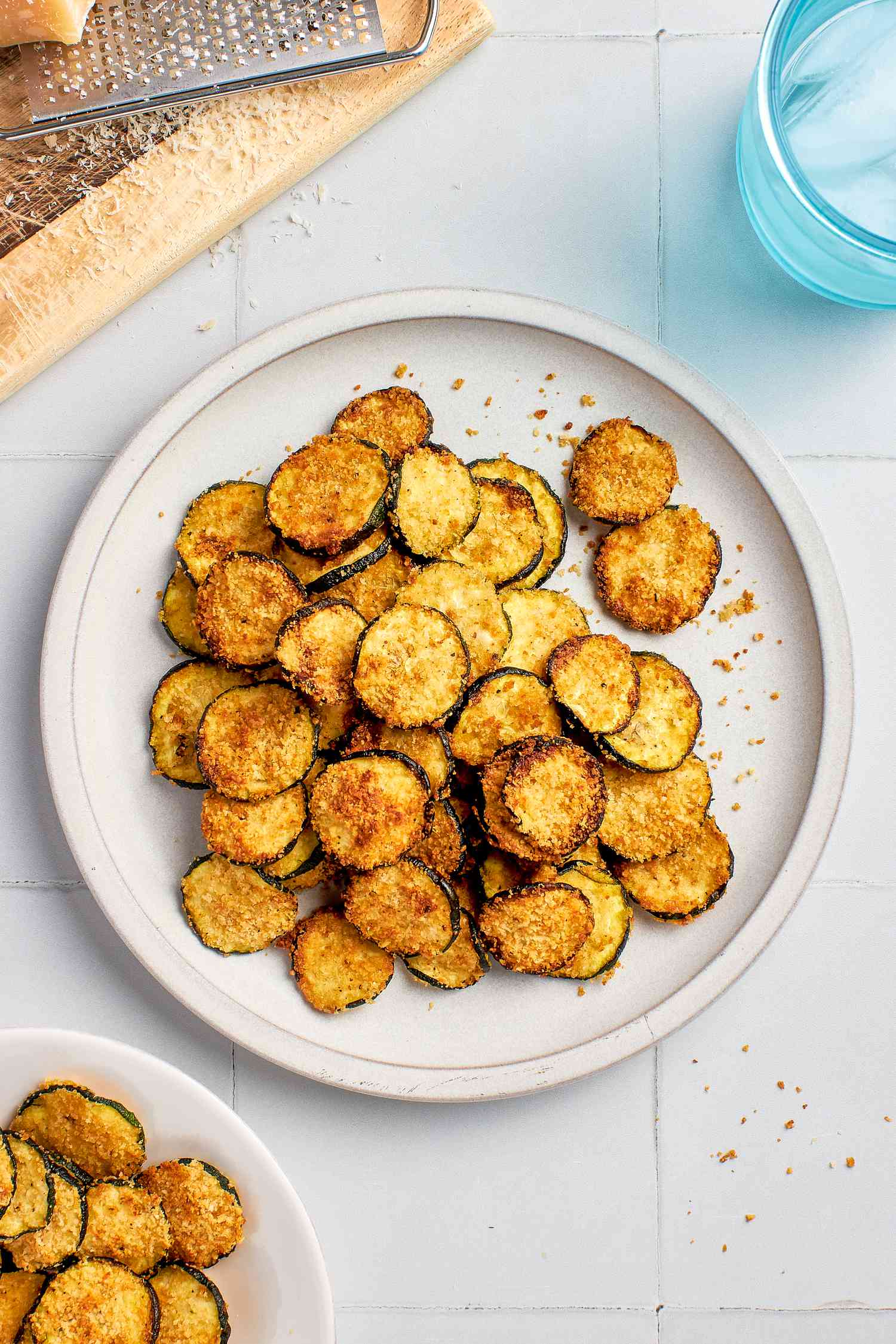Air fried zucchini slices on a plate with a block of Parmesan and a grater on the side