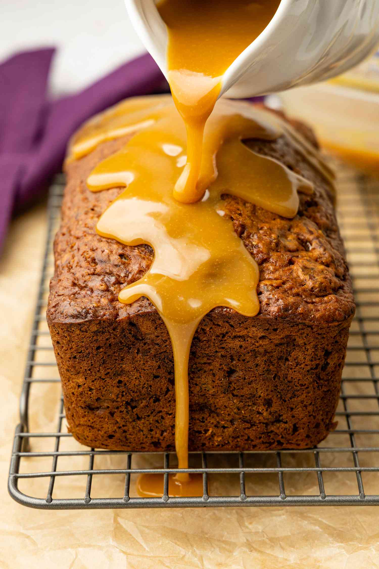 Pitcher of Caramelized White Chocolate Poured Onto a Loaf of Banana Pecan Bread on a Cooling Rack