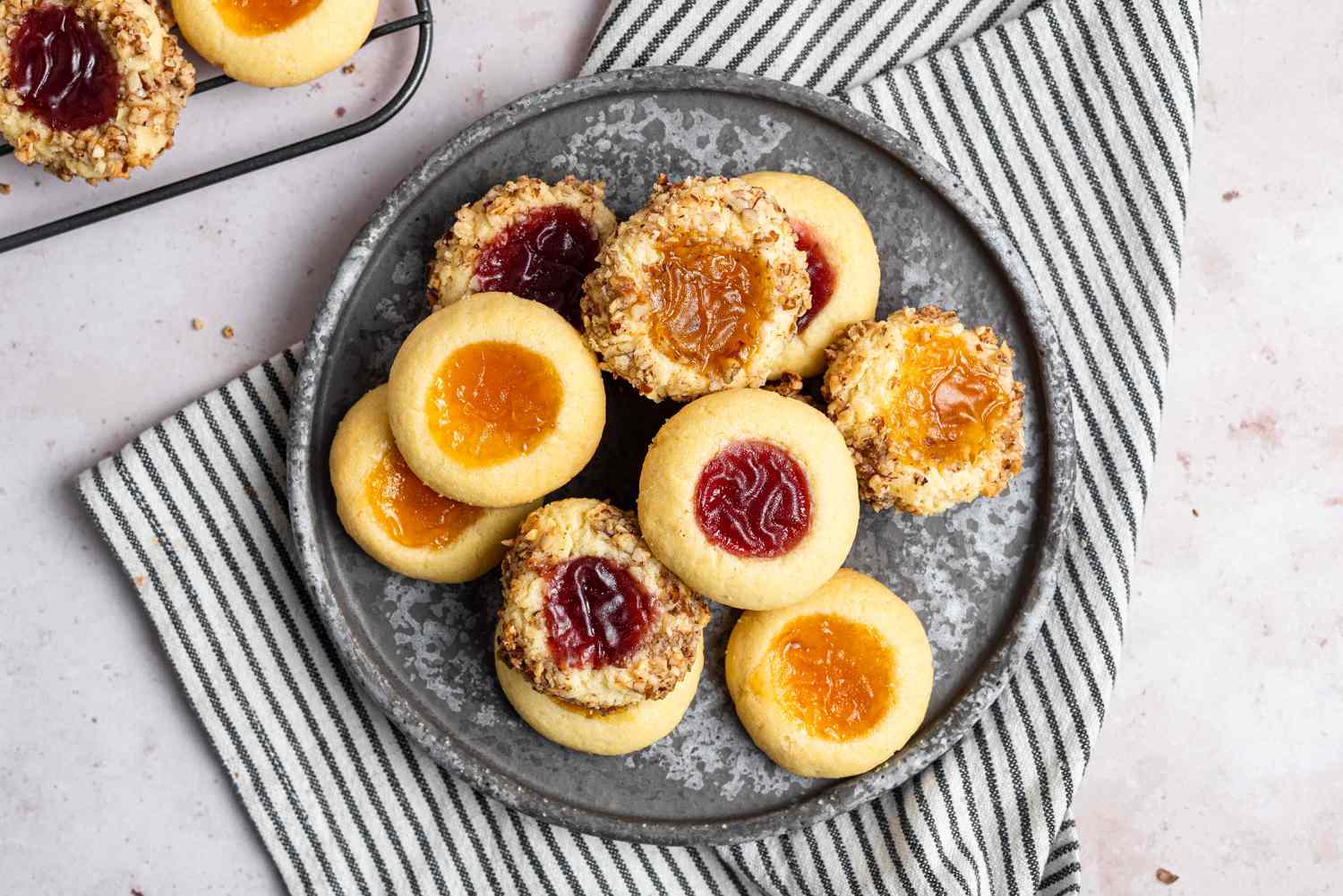 Overhead view of a plate of thumbprint cookies with a striped linen underneath.