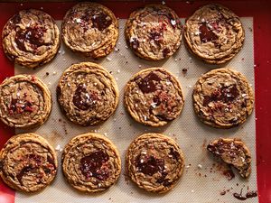 Freshly baked cookies on a baking sheet with a nonstick liner topped with chocolate chunks and flaky salt