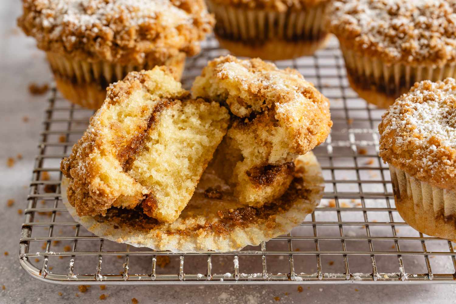 Coffee cake muffins with a crumb topping one cut open to reveal its texture on a cooling rack