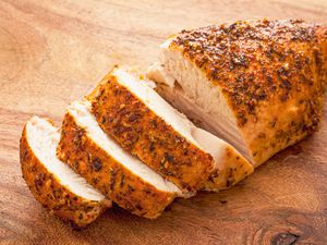 Moist and tender-looking spice-rubbed chicken breast partially sliced on a cutting board
