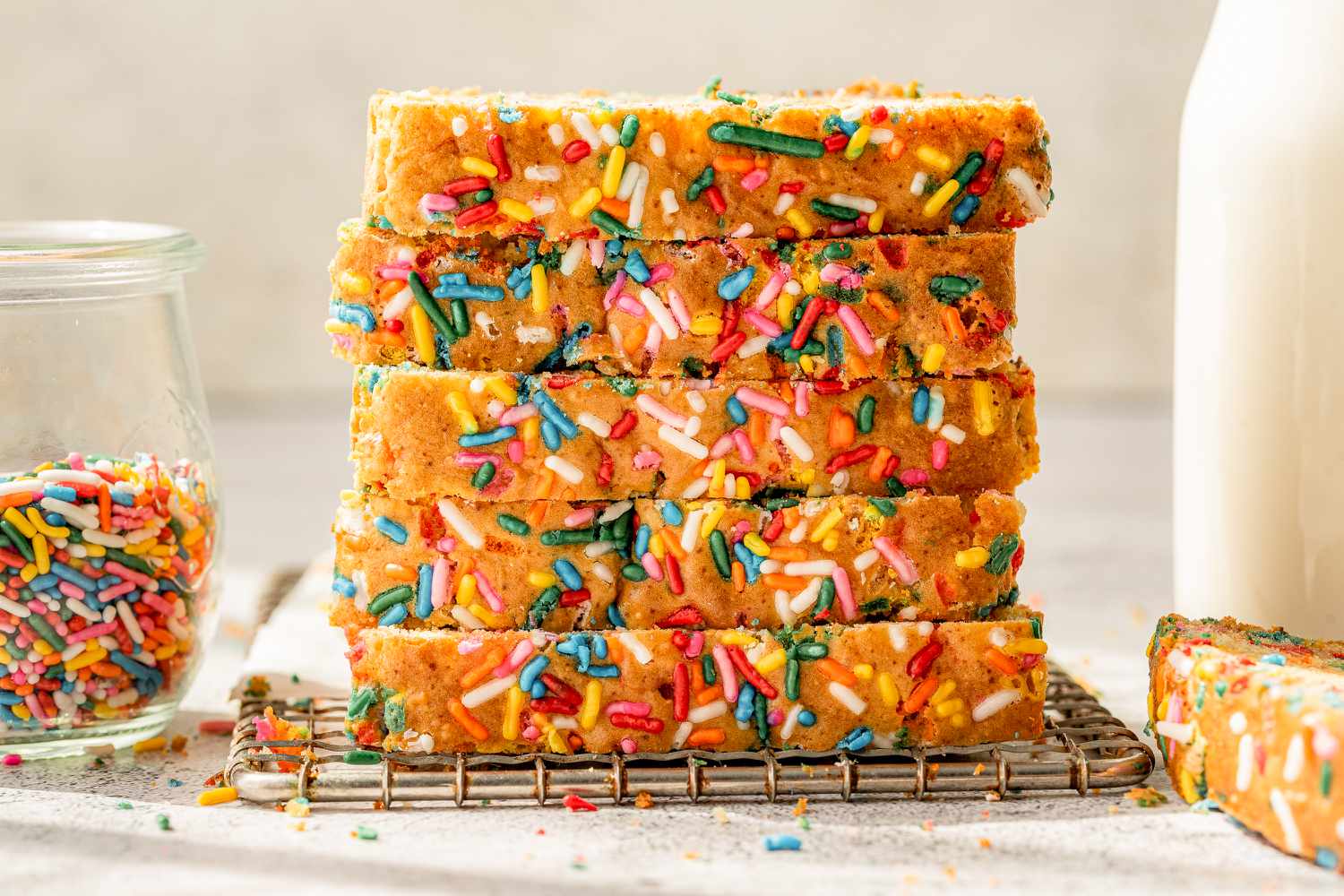 stack of sliced ice cream bread on a wire rack, and in the surroundings, a jar of sprinkles and a jar of milk