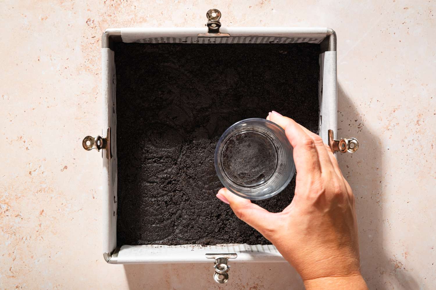 Overhead view of a flat-bottomed measuring cup pressing the crust into the bottom of a pan for Chocolate Delight recipe