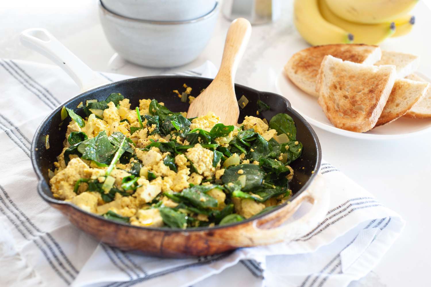 Vegan spinach and tofu scramble in skillet with toast on side.
