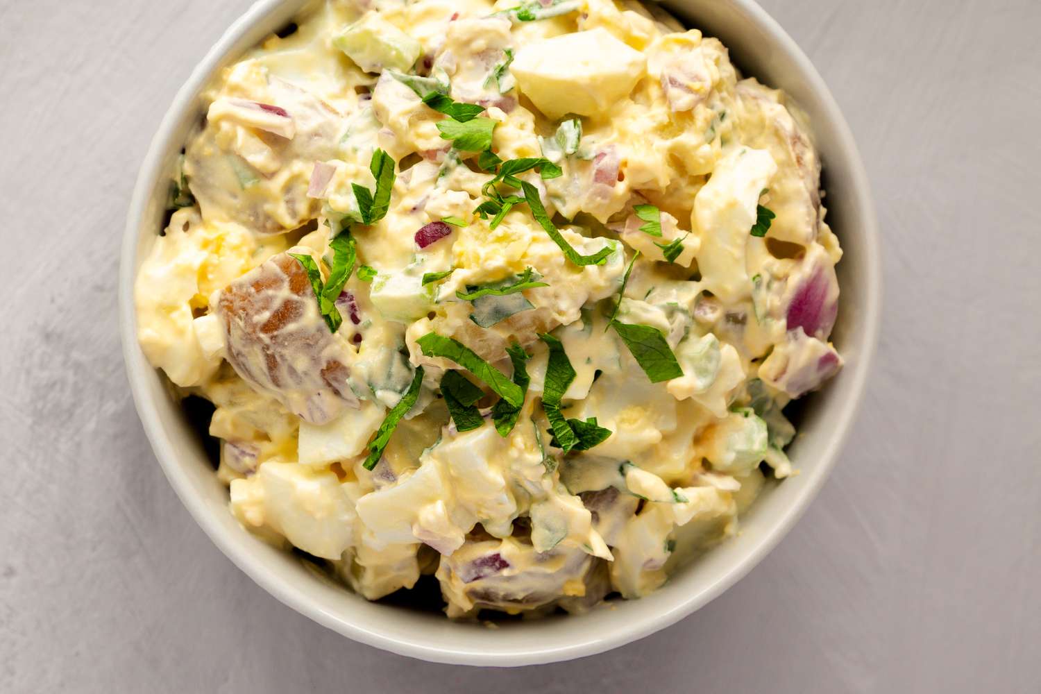 A bowl of creamy potato salad with herbs on top