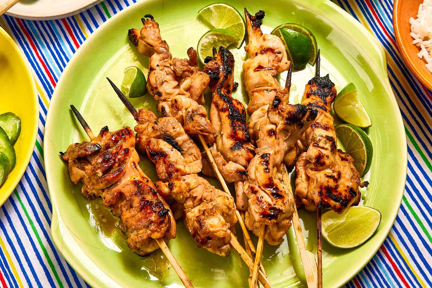 Grilled chicken skewers served on a green plate with lime wedges