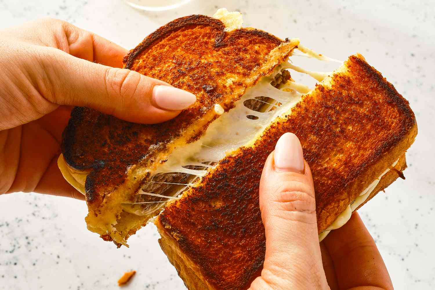 Hands pulling apart a patty melt sandwich with melted cheese stretching between the pieces