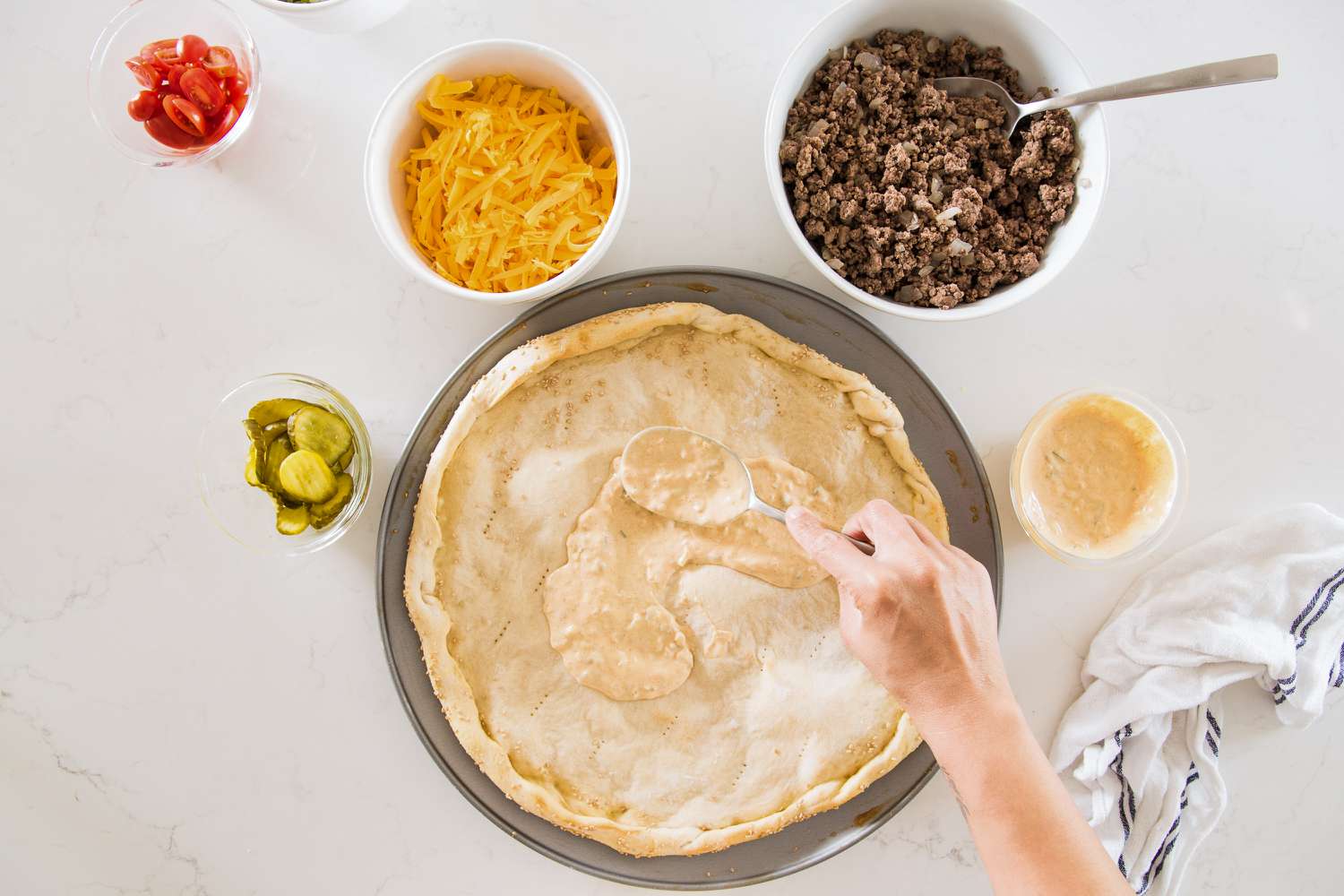 Special Sauce Spread onto Par-Baked Cheeseburger Pizza Crust, and Surrounding the Pizza Pan, Bowls of Toppings