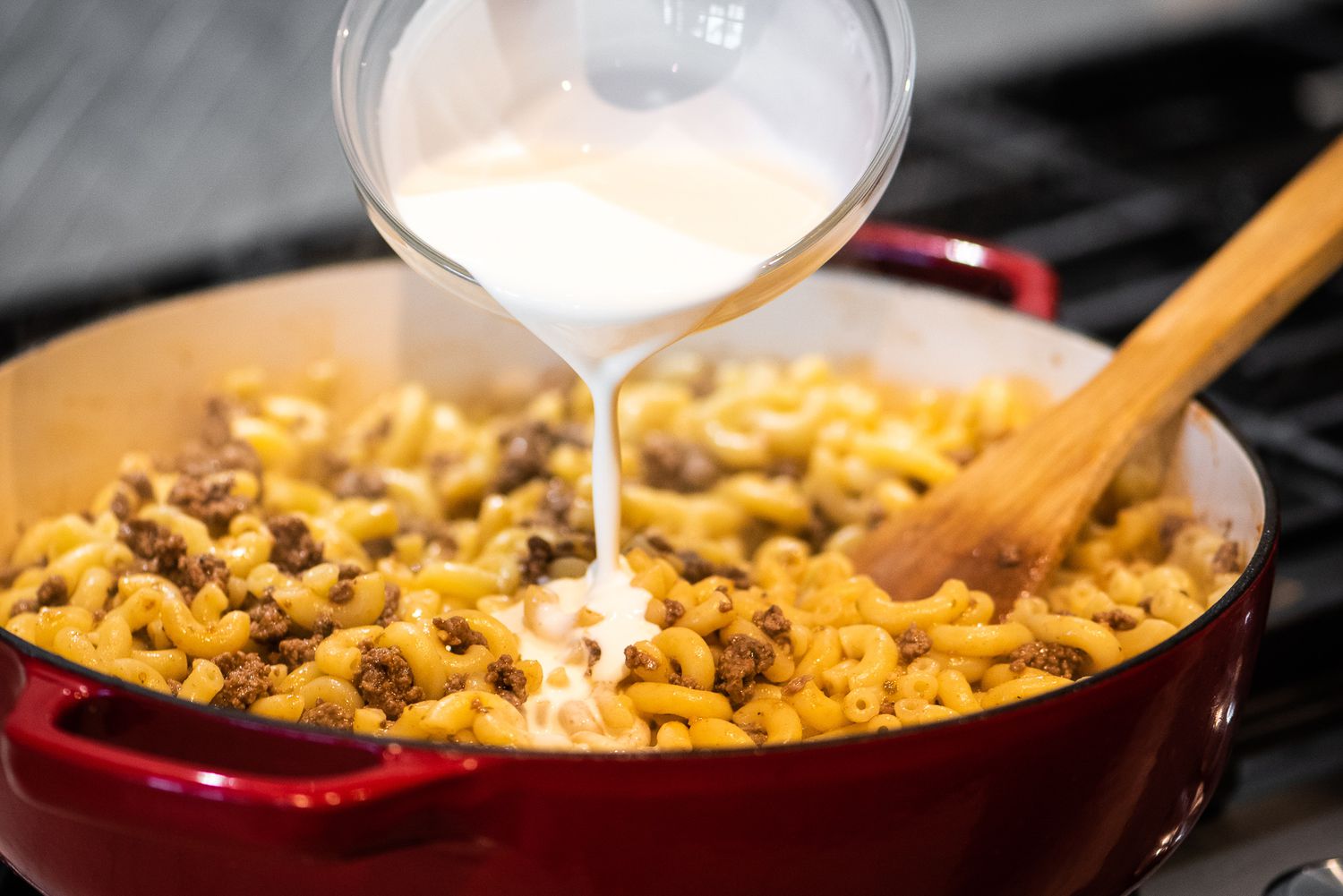 Bowl of Heavy Cream Poured into Dutch Oven with Cheeseburger Casserole Ingredients 
