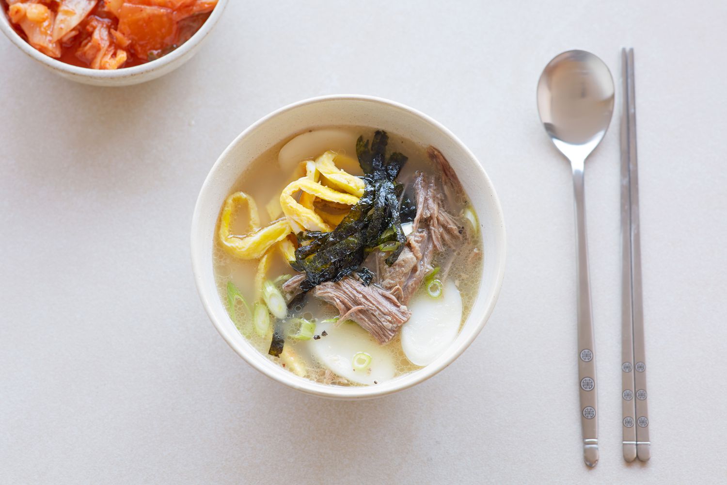 Overhead view of Korean rice cake soup on a table with a spoon.