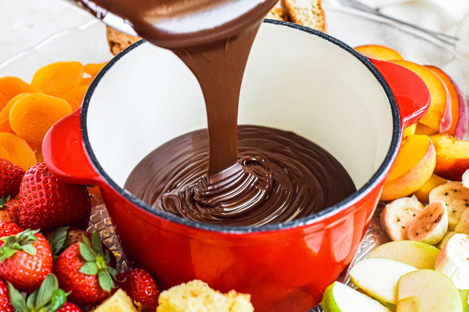Fondue chocolate poured into a small pot surrounded by cut fruit