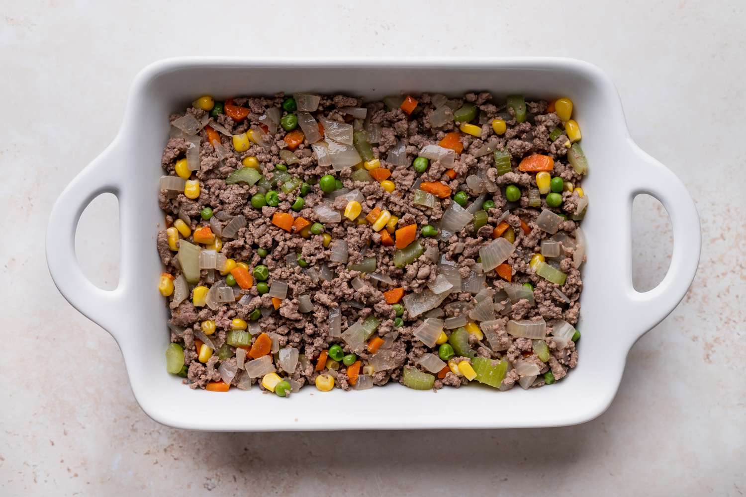 Overhead view of the ground beef filling for shepherds pie in a white casserole dish.