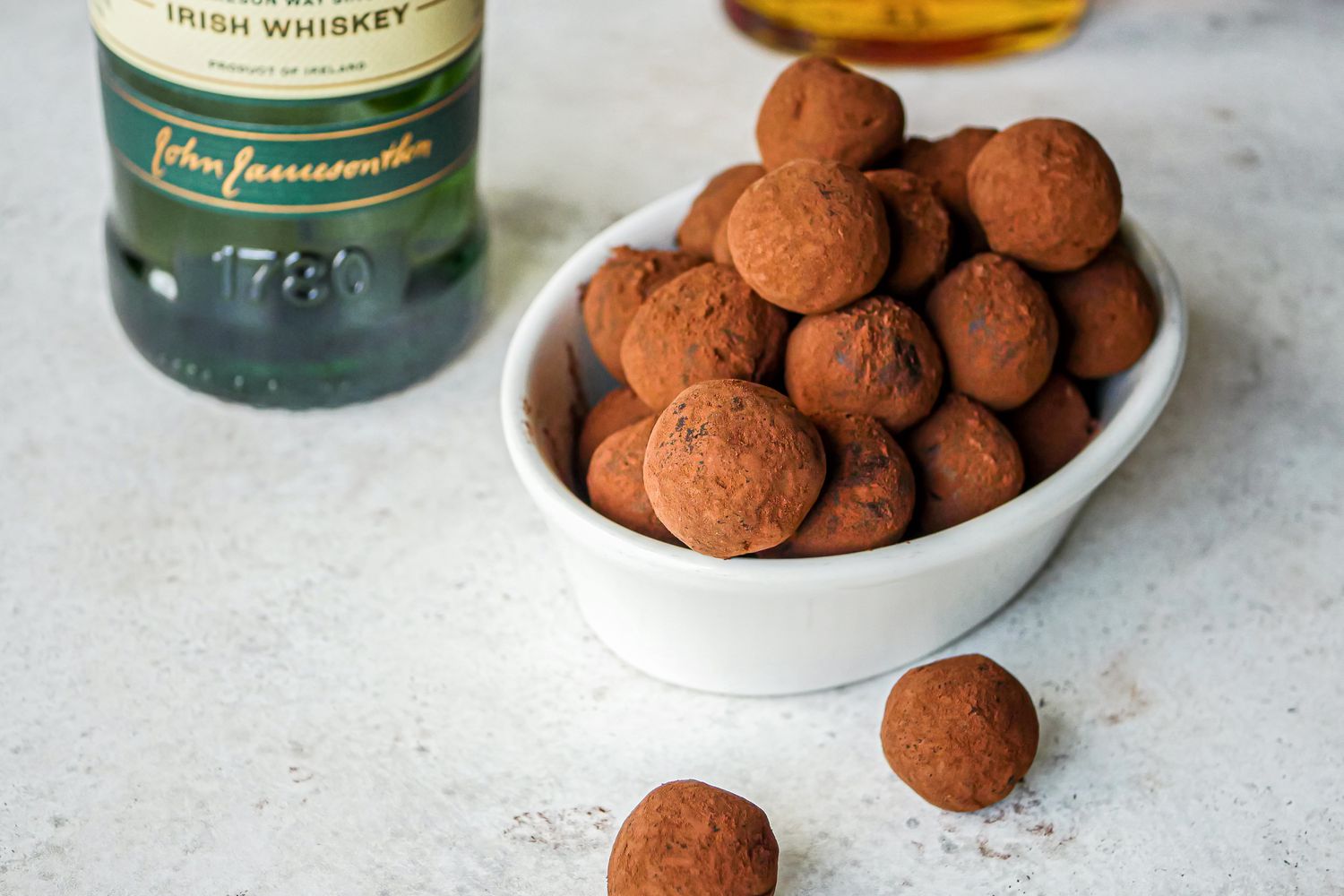 Whiskey Chocolate Truffles with bottles of whiskey behind a bowl filled with truffles.