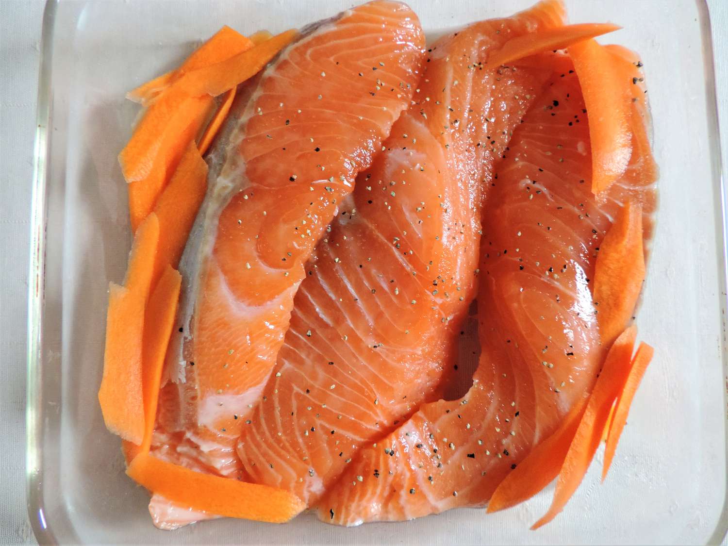 Raw salmon slices in a clear glass cooking pan