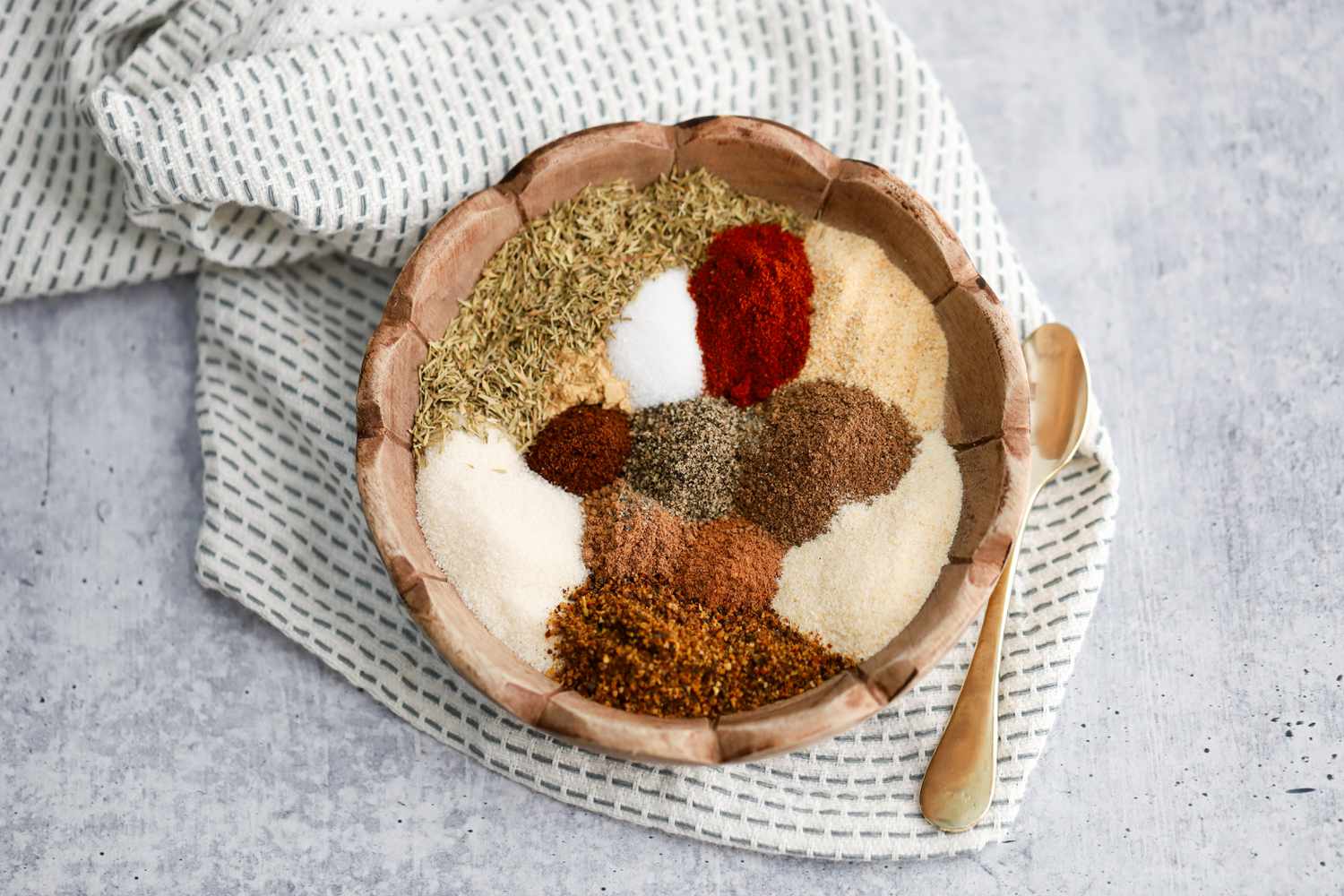 Bowl With Small Piles of Jerk Seasoning Ingredients Sitting on a Kitchen Towel Next to a Spoon