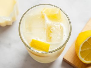A glass of creamy lemonade next to a halved lemon and lemon zest