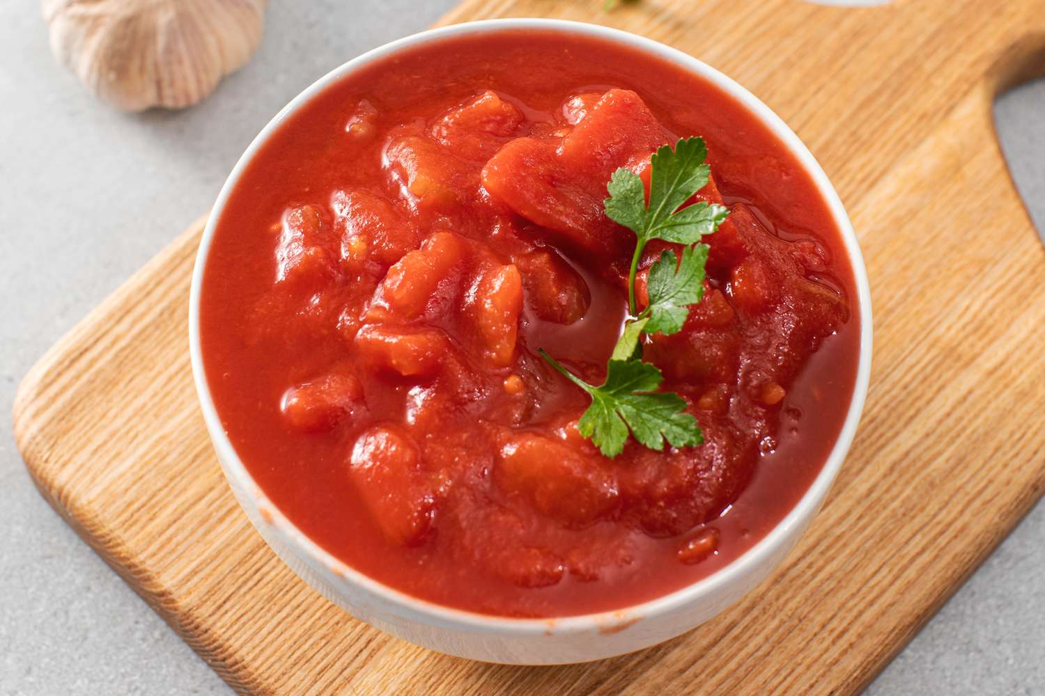 A bowl of canned tomatoes garnished with parsley on a wooden board