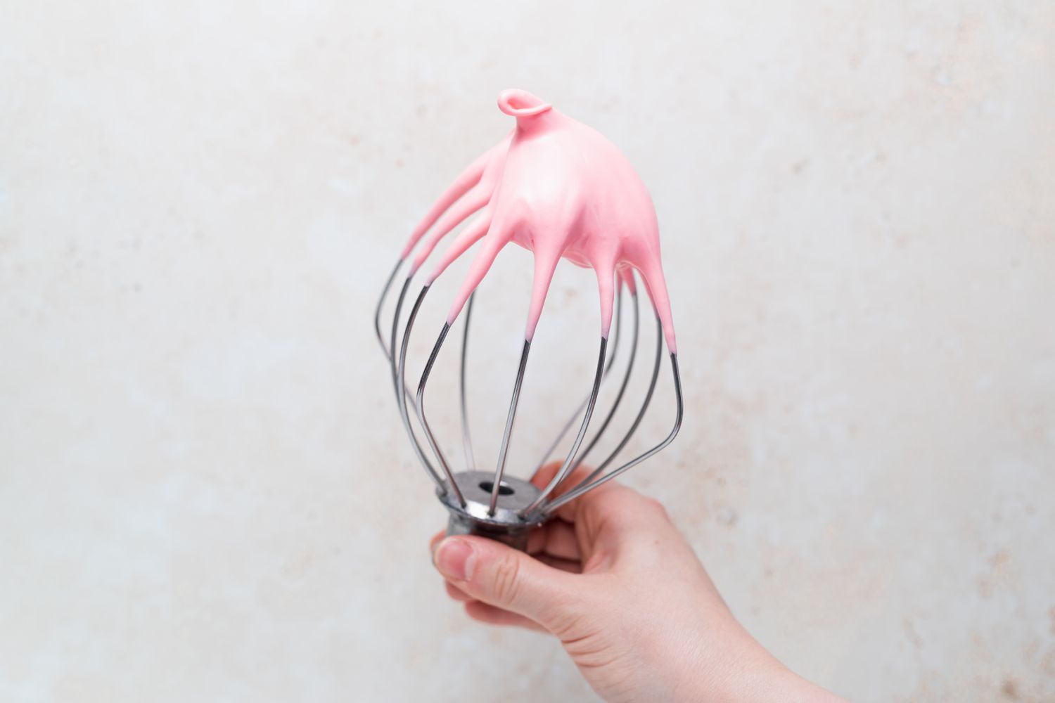 Pink meringue on a whisk to make raspberry macarons filled with raspberry buttercream