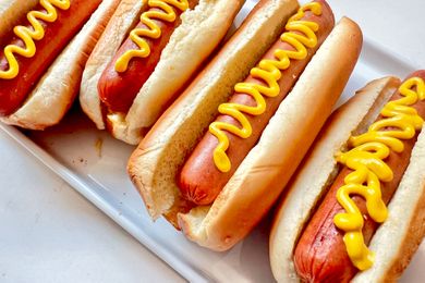 Four hot dogs in buns each topped with mustard