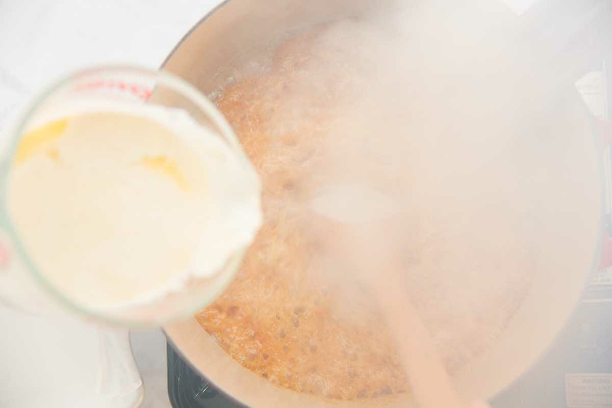 Warm cream being added to a steaming pot to show how to amke soft and chewy caramels.