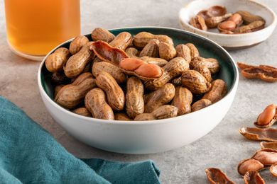 A bowl of boiled peanuts on a table with shelled boiled peanuts in the background